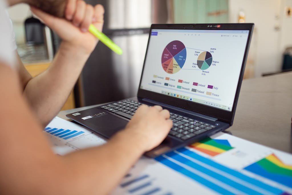Person leveraging AI Business Automation to analyze financial data on a laptop with colorful documents, showcasing market analysis.